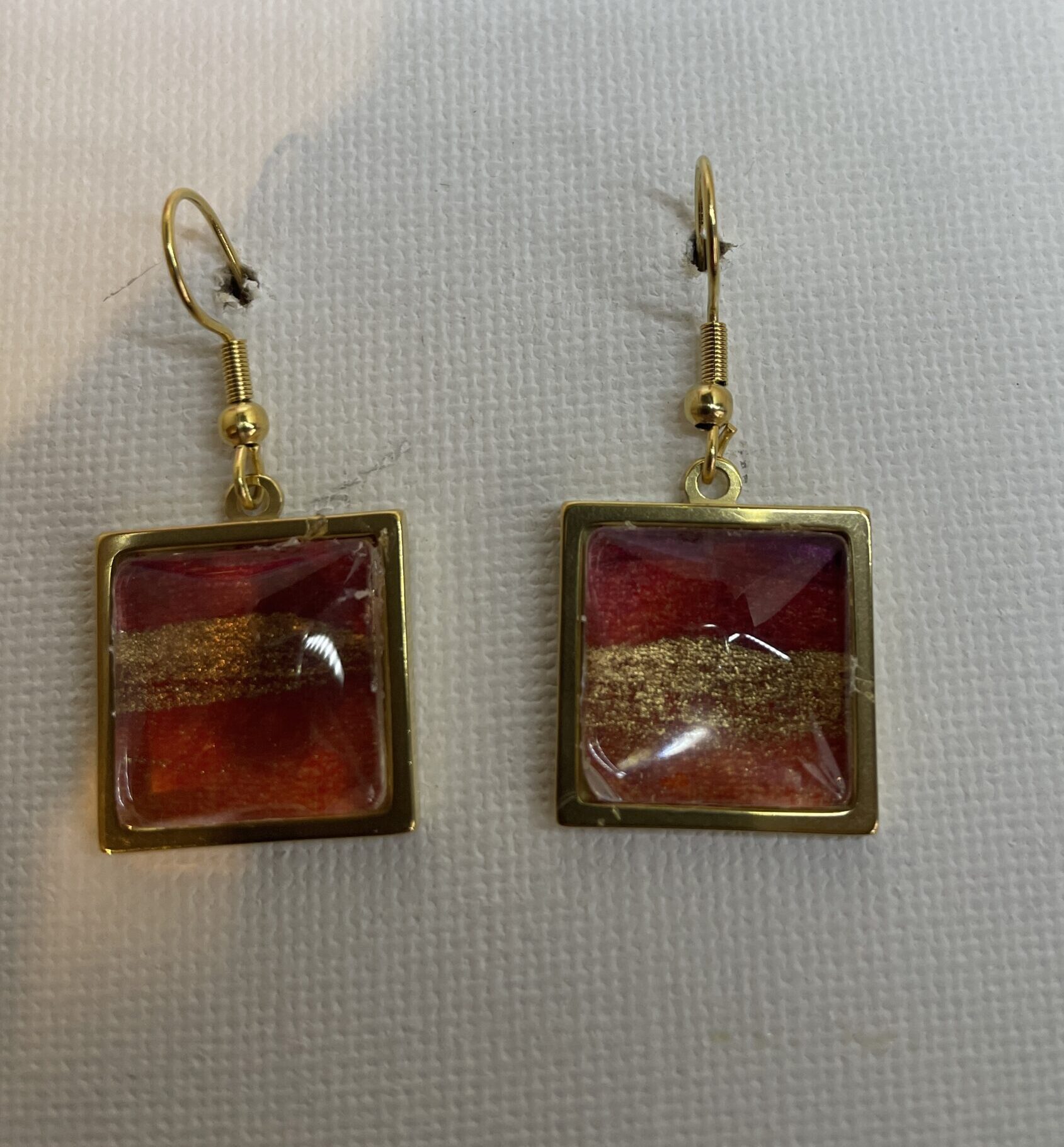 Earrings: square gold coloured metal setting featuring red and gold ink beneath a glass cabouchon