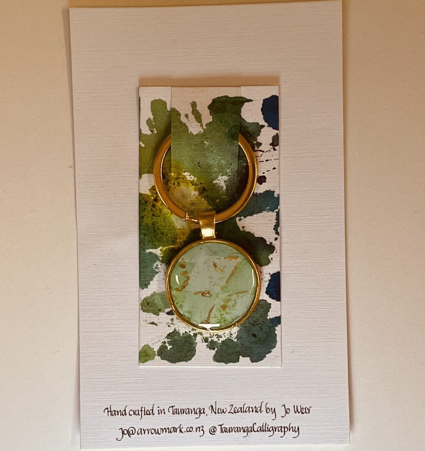 Hand crafted key ring featuring green and gold ink beneath a resin dome.