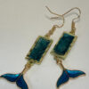 Hand crafted earrings made from colour-shift paint, alcohol ink and resin, set in gold bezels and featuring metallic blue and gold coloured whale tails.