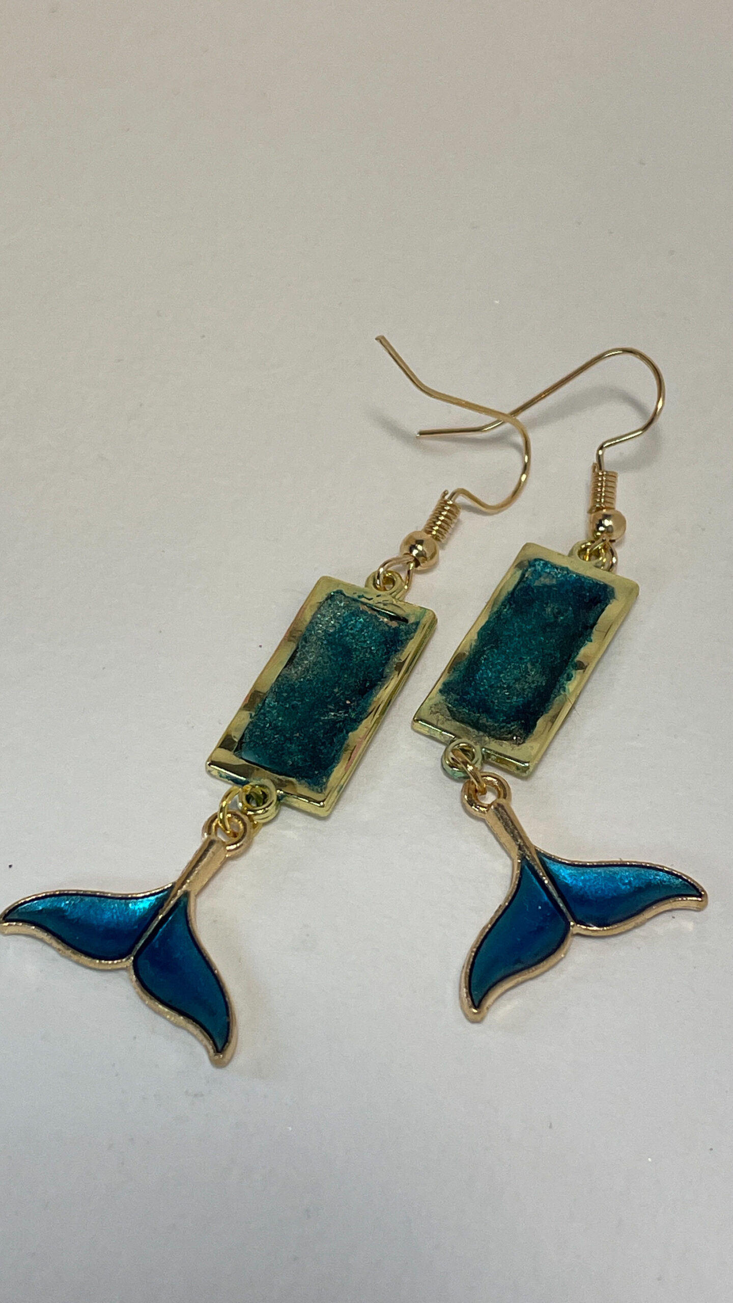 Hand crafted earrings made from colour-shift paint, alcohol ink and resin, set in gold bezels and featuring metallic blue and gold coloured whale tails.