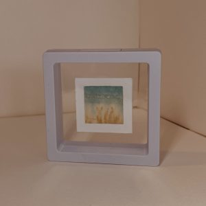 Reverse view of miniature landscape painted by hand on delicate tissue paper which is mounted within a card frame and within a transparent plastic click-frame. Gentle green and teal inks.