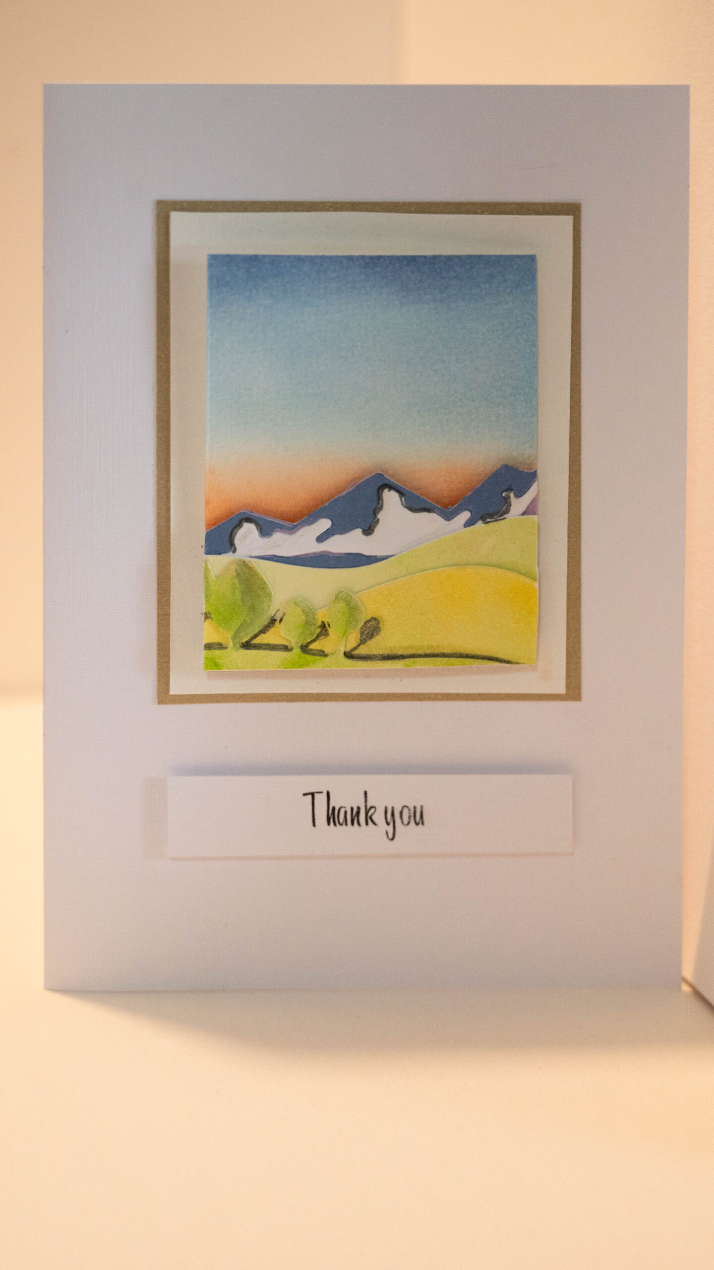 Hand crafted thank you card featuring a hand painted sunset backdrop with 3D mountains, hills and trees. 
