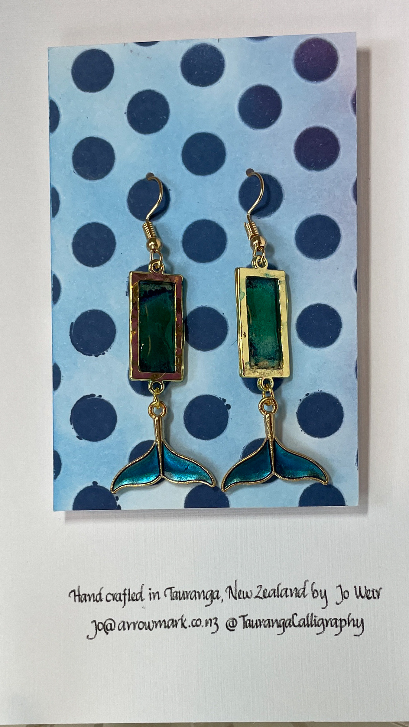 Hand crafted earrings made from colour-shift paint, alcohol ink and resin, set in gold bezels and featuring metallic blue and gold coloured whale tails.