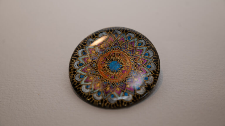 Tauranga Jewellery: Brooch featuring gold embossed mandala hand coloured with blue and orange chameleon paints and protected with resin layers