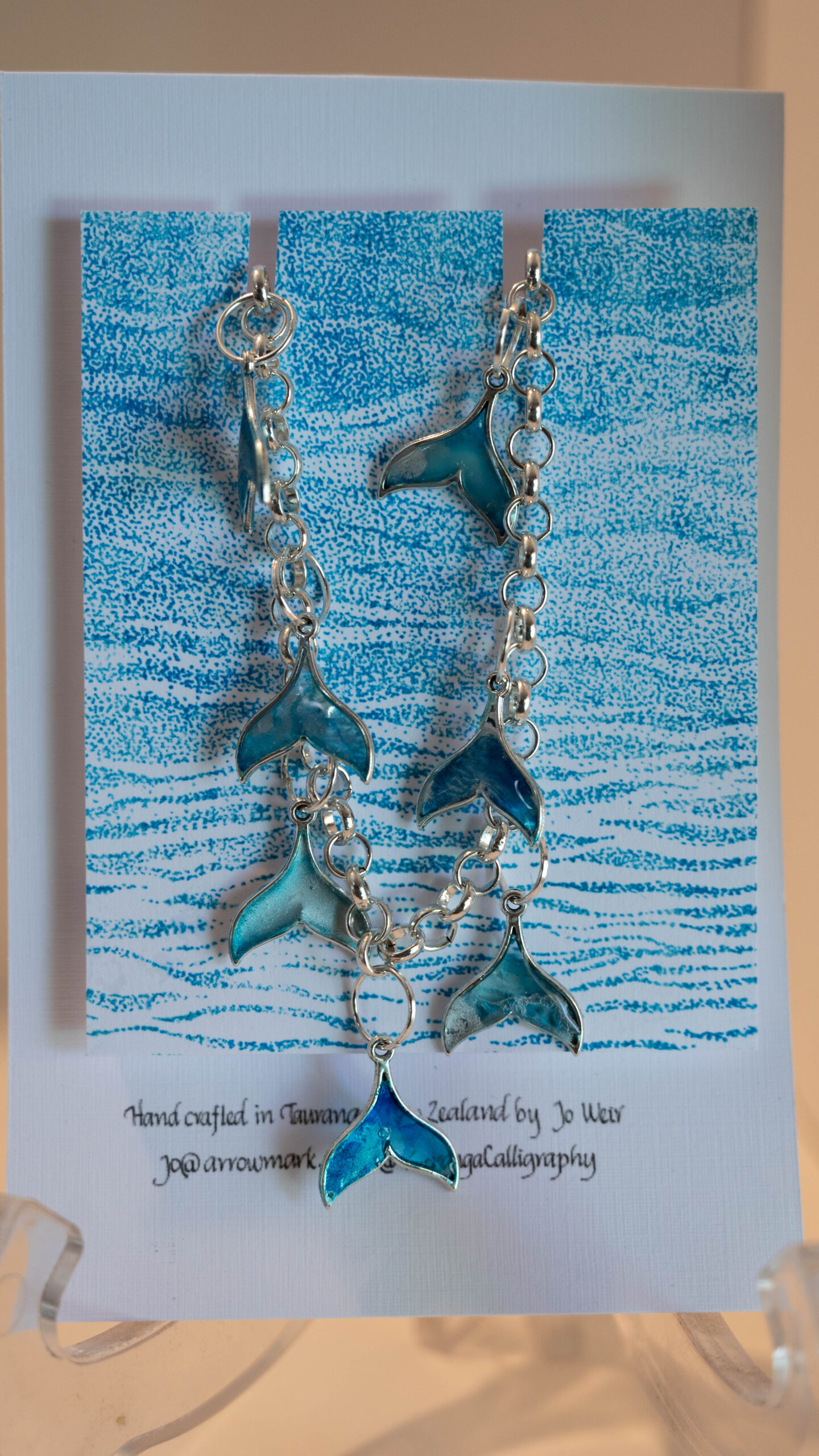 Jewellery: Whale Tail Necklace. Silver-coloured ink and resin whale tails hand crafted and hung from a silver coloured chain link necklace.