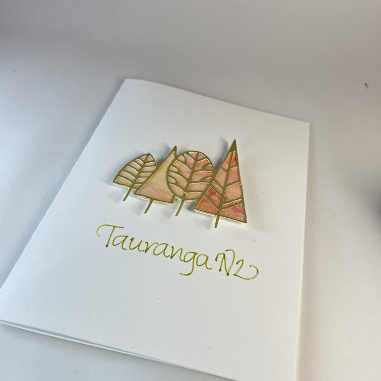 Hand made greeting card featuring four die cut gold trees filled with alcohol ink art and calligraphy text "Tauranga, NZ".