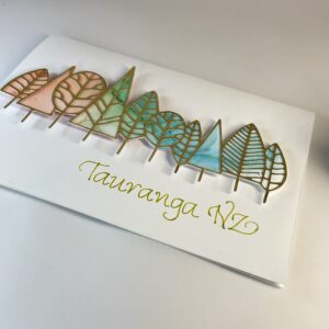 Hand made greeting card featuring die cut gold trees filled with alcohol ink art and calligraphy text "Tauranga, NZ".