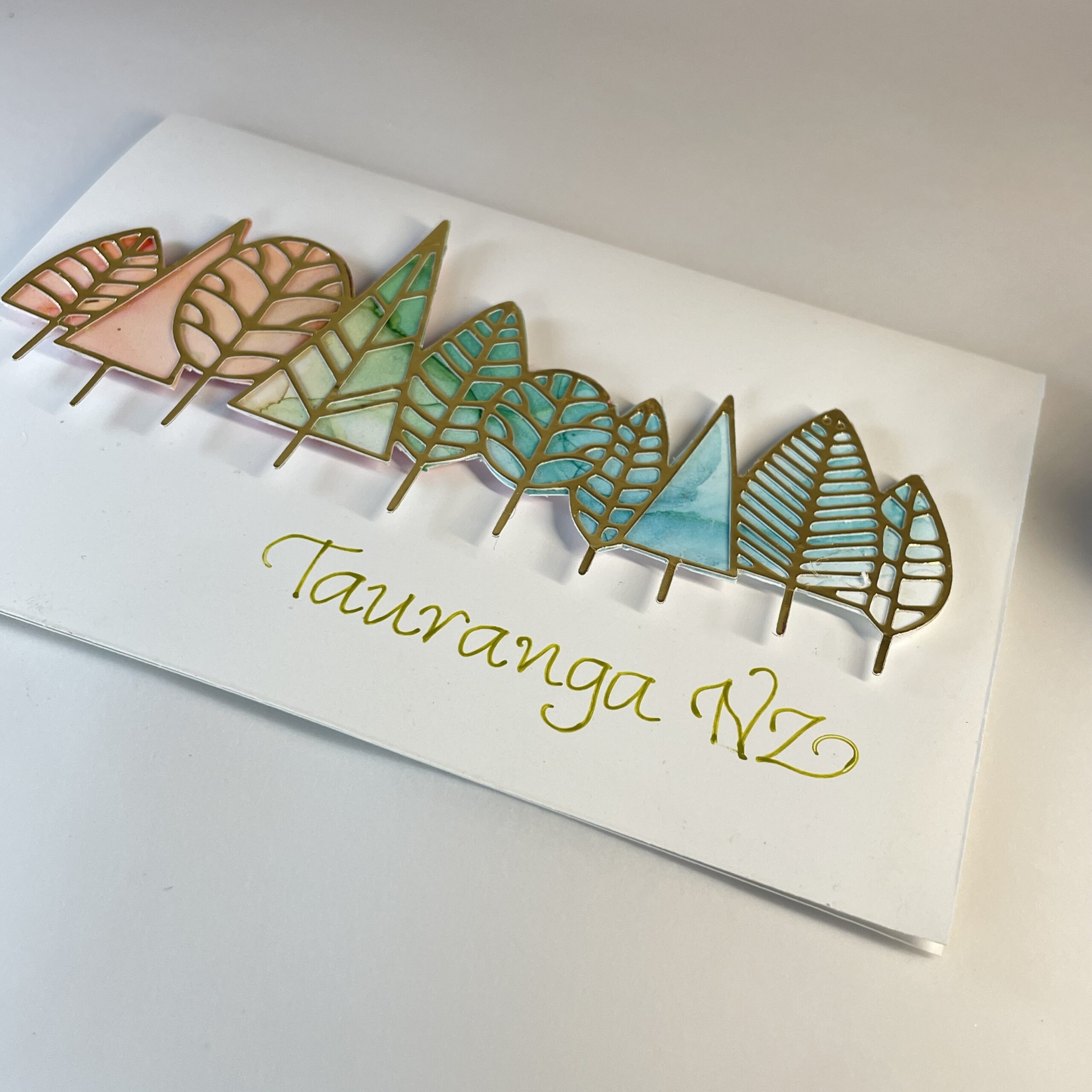 Hand made greeting card Hand made greeting card featuring die cut gold trees filled with alcohol ink art and calligraphy text "Tauranga, NZ".