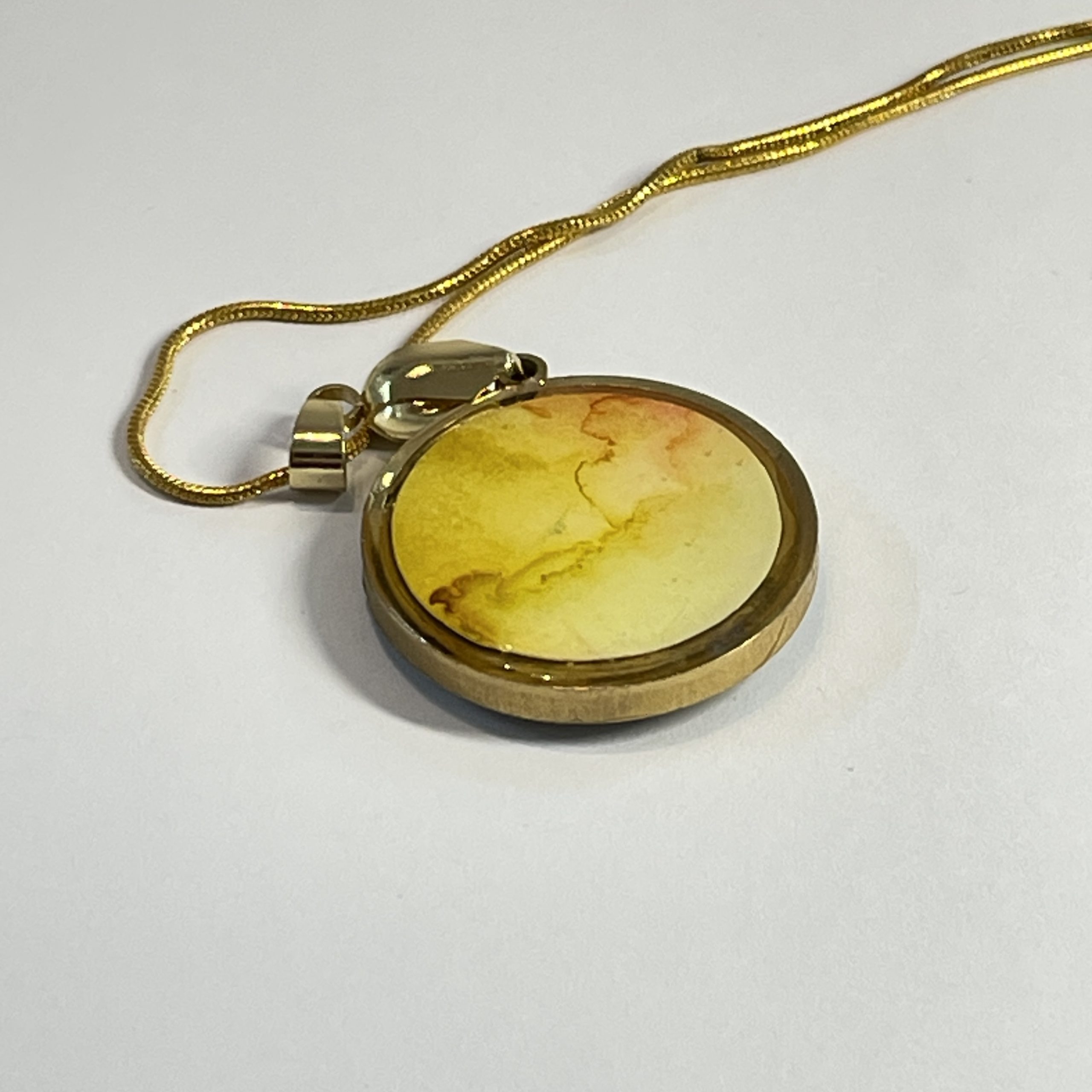 Pendant: double sided round pendant, each side containing a round piece of hand painted and embossed paper, yellow one side, blue the other