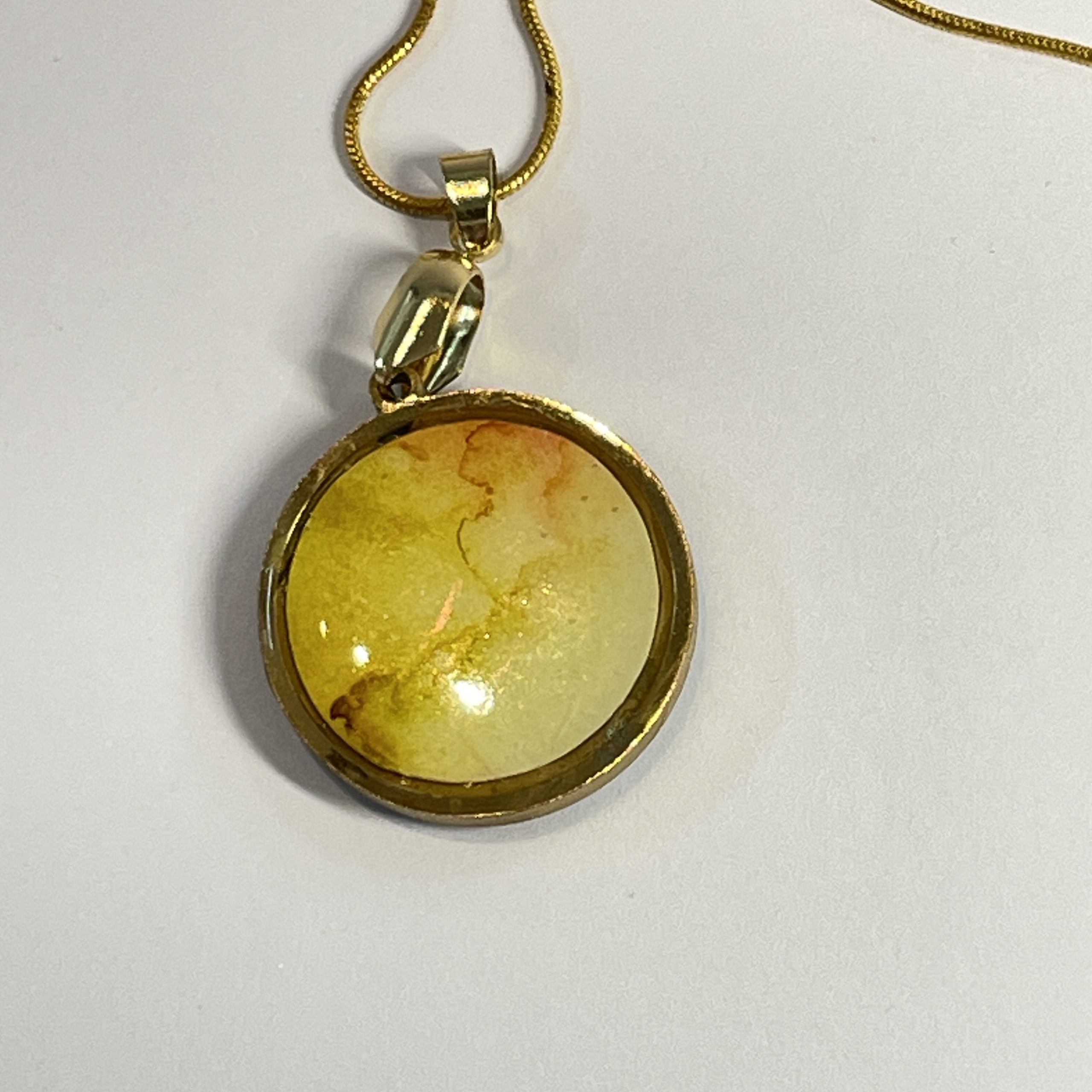 Pendant: double sided round pendant, each side containing a round piece of hand painted and embossed paper, yellow one side, blue the other