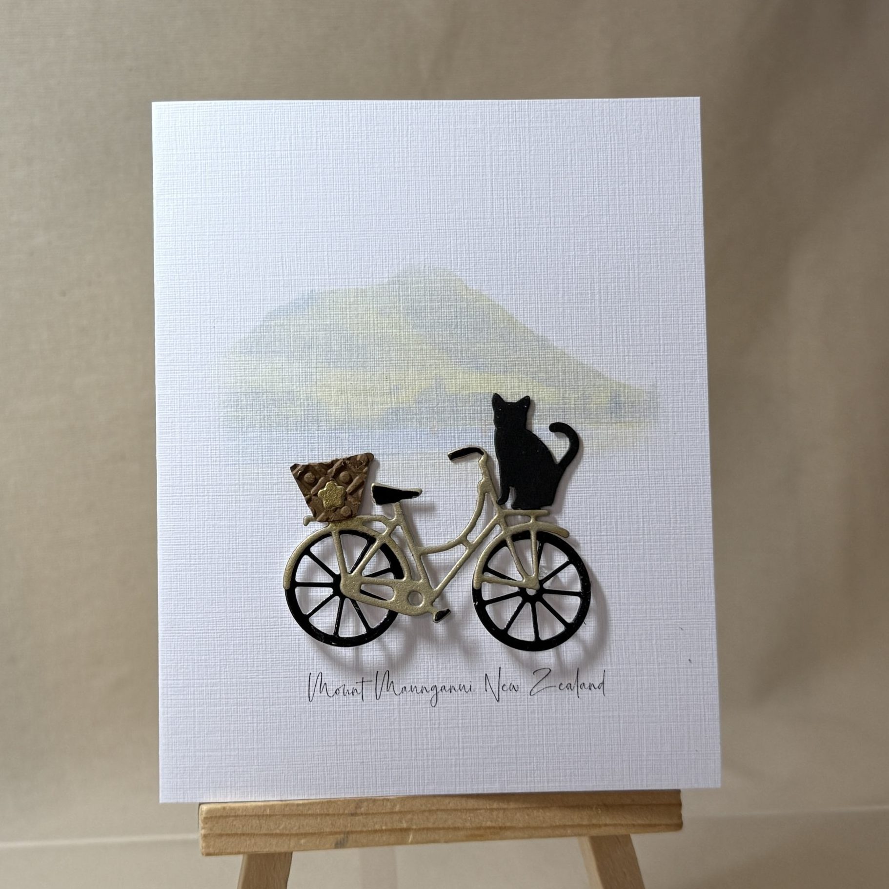 Mount Maunganui greeting card featuring a hand made bicycle with a basket and a black cat